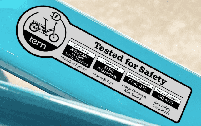 Close-up of an e-bike safety certification label showing compliance with ANSI/CAN/UL 2849, CPSC 1512, and ISO 4210 standards for electrical, frame, and bicycle safety.